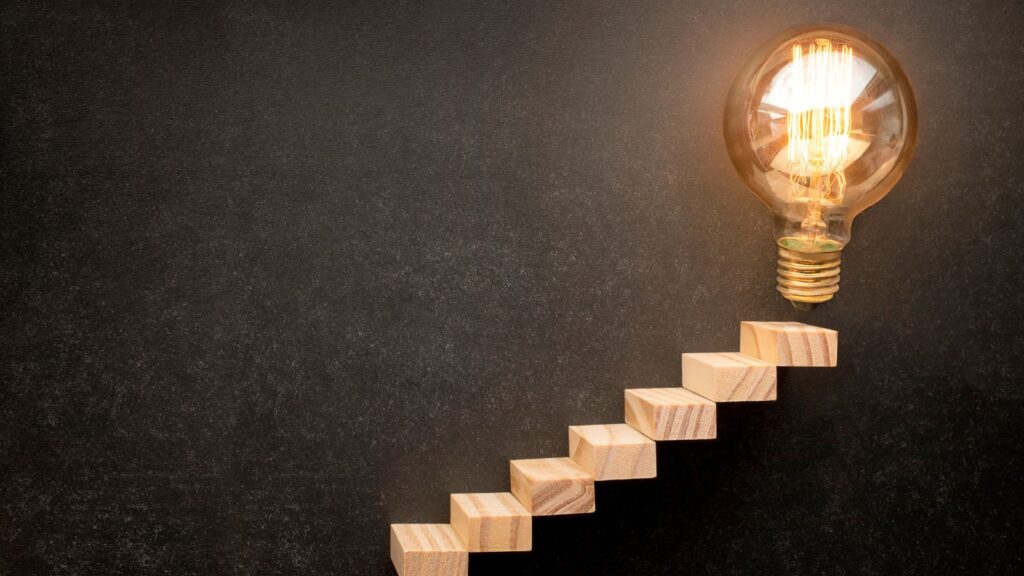 Wooden blocks forming steps leading to a glowing lightbulb, symbolizing progress and innovation in an ERP Migration Roadmap to Microsoft Dynamics 365 Business Central.