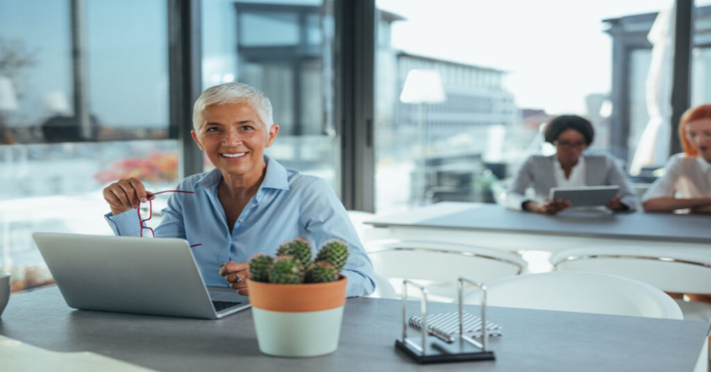A woman is productive on her laptop in an office with some workers in the background reviewing AI in Microsoft Dynamics 365 Business Central.