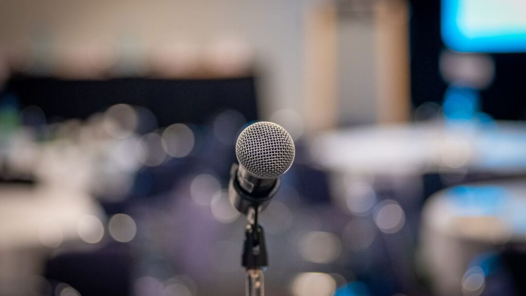 Microphone on a stand in focus with a blurred background of a conference room, ready for a session on Business Central Training at a professional event.
