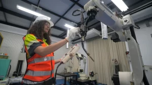Engineer operating a robotic arm using a handheld controller in a modern manufacturing lab, demonstrating Advanced Shop Floor Integrations and automation technologies in action.