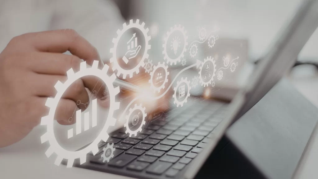 Quality management and process optimization concept shown by a professional using a laptop with digital gear and analytics icons representing performance tracking, workflow automation, and continuous improvement.